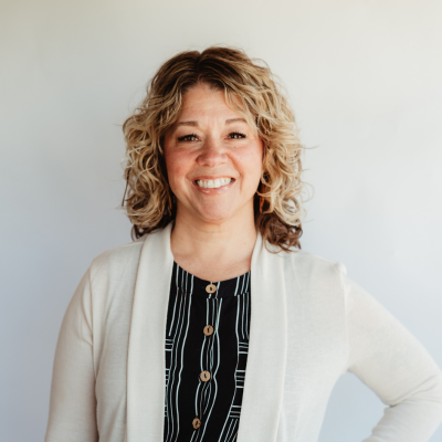 Jackie Clendenen smiling confidently in a light cardigan and patterned top against a neutral background.